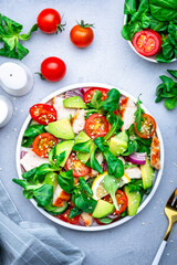 Fresh salad with avocado, chicken, tomatoes and lettuce, gray background, top view