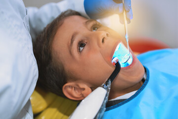 Fototapeta premium Hands, child and dental curing light for cleaning teeth, health and oral hygiene at pediatric clinic. Boy, dentist and uv treatment for tooth, closeup and orthodontics tools for filling cavity or dry