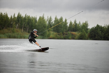 Wide angle side view of man enjoying action water sports and wakeboarding on scenic forest lake...