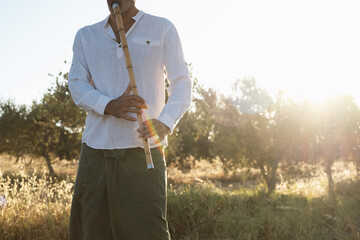 Portrait of a man playing ney flute in an olive field