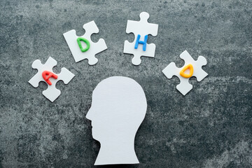 Head silhouette surrounded by puzzle pieces labeled ADHD, emphasizing awareness and understanding...
