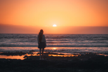 Fototapeta premium Silhouette of a person standing on the beach at sunset with vibrant colors