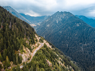 Aerial view of a mountain road winding through lush green hills, surrounded by cloudy skies.