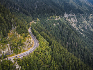 Aerial view of green mountains with a winding road and dramatic cloudy skies above.