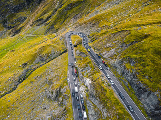 Aerial drone view of the Transfagarasan highway in autumn, featuring winding roads and colorful foliage with cars navigating the scenic route.