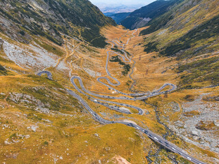 Aerial shot of the Transfagarasan road with vehicles, surrounded by stunning autumn foliage.