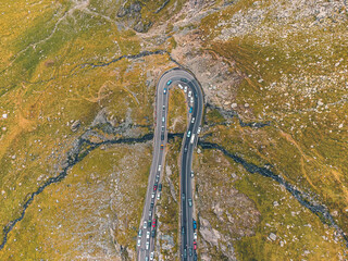  Drone perspective of the Transfagarasan highway during fall, featuring colorful trees and cars traversing the curves.