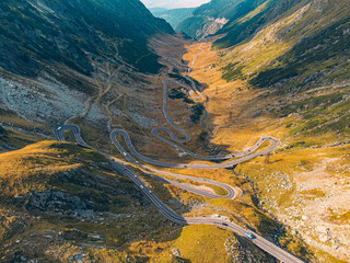 Aerial view of the winding Transfagarasan highway in autumn, with a mix of vehicles and golden leaves.