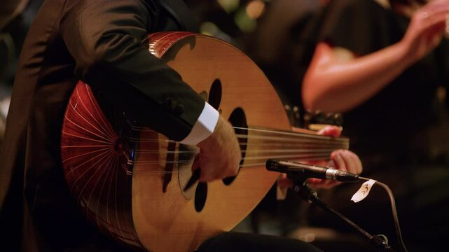Steady shot of a male musician playing Oud instrument in an orchestra concert.