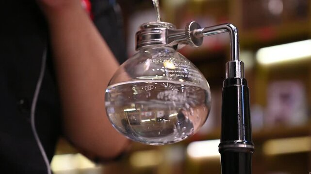 Barista pours water into a coffee syphon brewer