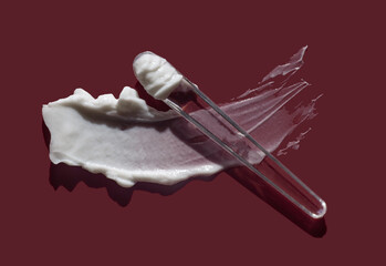 Cosmetic cream butter smudge swatch with glass applicator stick isolated on rich burgundy background