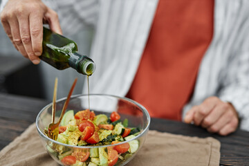 Close up of unrecognizable man pouring virgin olive oil as dressing for fresh homemade salad enjoying lunch at outdoor terrace copy space