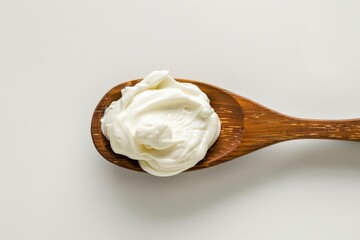 A wooden spoon filled with whipped cream on a white surface, ready for use in baking or decorating