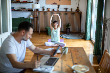 Woman practicing yoga while man works on laptop at home