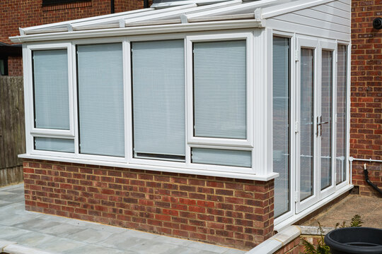 White lean to conservatory with blinds on all windows and doors, seen from the outside on a sunny day.