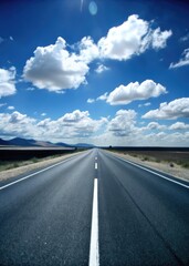 Fototapeta premium Long open road leading towards a horizon filled with fluffy clouds.