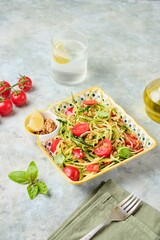 Healthy salad, zucchini spaghetti with cherry tomatoes and walnuts in a colorful plate on a gray concrete background. Vegan recipes.
