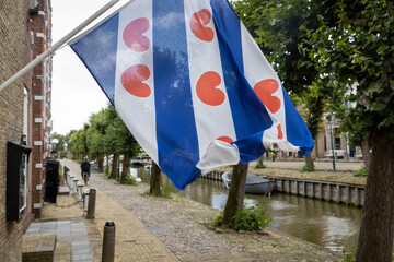 Close up of a Frisian flag in the town of Sloten with a cityscape with a canal and cyclist in the background