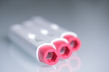 Detail of the heads of three pen injectors with a red tip for biological treatments such as Adalimumab, Etanercept or epinephrine. The background is unfocused, aseptic, clean, white and well lit.