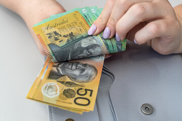 Female hands holding australian dollars into grey purse. Saving conept