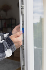a man's hand lowers an iron part in a window frame.
switching windows to autumn-winter mode, insulating an apartment. seasonal cold snap