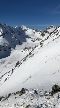 View from Patria, Vysoke Tatry, High Tatras, Slovakia. Landscape of beautiful peak, summit and top. Nature in winter. Sunny, blue sky and snow. Panoramatic panning vertical video. People shadow.