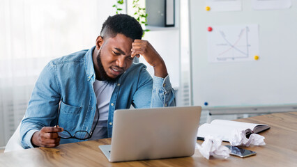 Creativity crisis. Stressed employee sitting at workplace and looking to laptop screen, unable to...