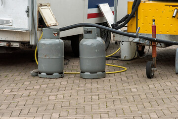 two gray steel gas bottles stand outside on the street next to a market stall