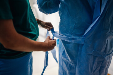 Close-up of hands tying blue medical gown in a surgical setting.