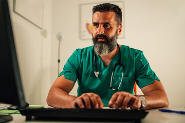 Doctor in green scrubs typing on computer at his medical office