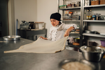 Young girl chef managing dough in a professional kitchen workspace.