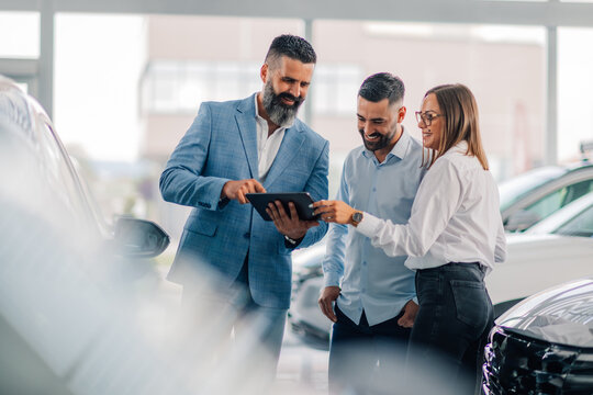 Showroom tablet consultation amid gleaming new automobiles.