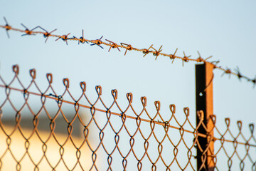 iron stake and a wire mesh fence with barbed wire against blue sky at evening