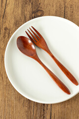 Fork and spoon on white empty plate with rustic wooden background. Top view. Concept of fasting and dieting.