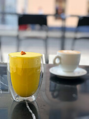 Bright yellow vegan smoothie with alternative plant milk with delicate floral accent on marble table. Vibrant drink with rich color and elegant presentation. Coffee Shop for vegetarian and cafe