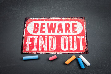Find Out. Beware sign with text and colored pieces of chalk on a dark chalkboard background