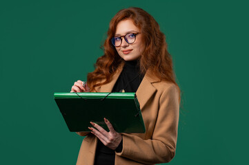 Young businesswoman writing notes in planner with pen. Lady boss thinking about future plans and to-do list in notebook for week, month, year. Keeping personal diary on green background