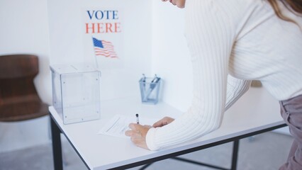 View from behind of Caucasian woman standing in front of white table and writing something with...