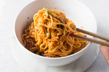 Spicy instant noodles with slices of green and red chili, spicy ramen noodles with chopsticks in a white ceramic bowl
