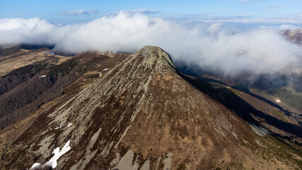 Sommet d'une montagne traversant les nuages. Pic montagneux jonch&eacute; par les plaques de neige en hiver. Sommet du Puy Griou per&ccedil;u depuis le ciel