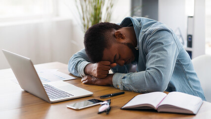 Naklejka premium Overworking concept. Tired african american businessman sleeping at workplace in office, exhausted after hard project