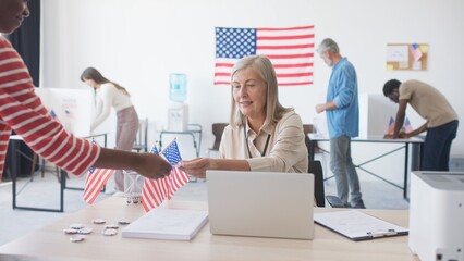 American citizens visiting local polling station. Smiling woman meeting voters while sitting at...