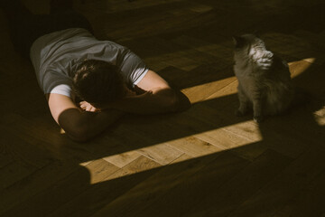 A young man lies on the floor next to a fluffy white Ragdoll cat