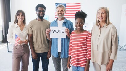 Multi-ethnic people in casual clothes standing next to each other. American office or state polling station. Man in middle holding paper with inscription 