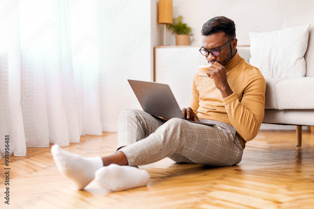 Poster busy afro freelancer guy using laptop computer working on weekend and having coffee sitting on floor