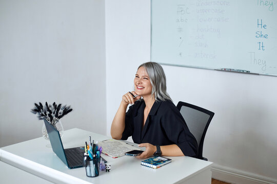 Portrait of a young beautiful English teacher working at school, at her desk in the classroom.