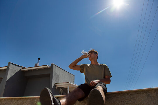Young man sitting grinking water against blue sky background