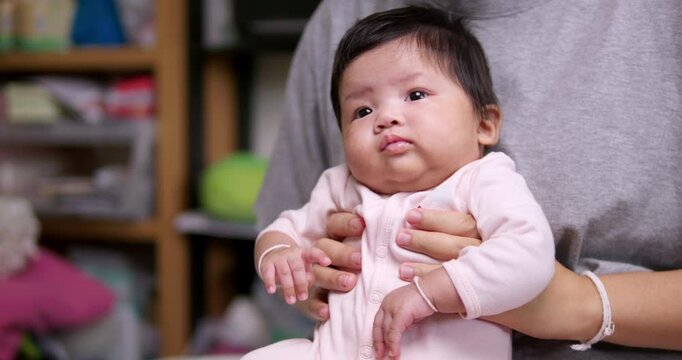 Sitting on her mother's lap, a newborn child begins to squirm and break into cries while flailing her arms.