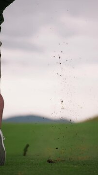 Golfer hitting wedge shot making big divot in slow motion, ball landing on green, vertical 4k golf footage