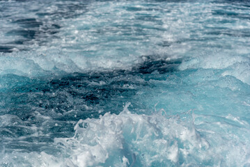 Turquoise blue ocean water foaming behind a ship